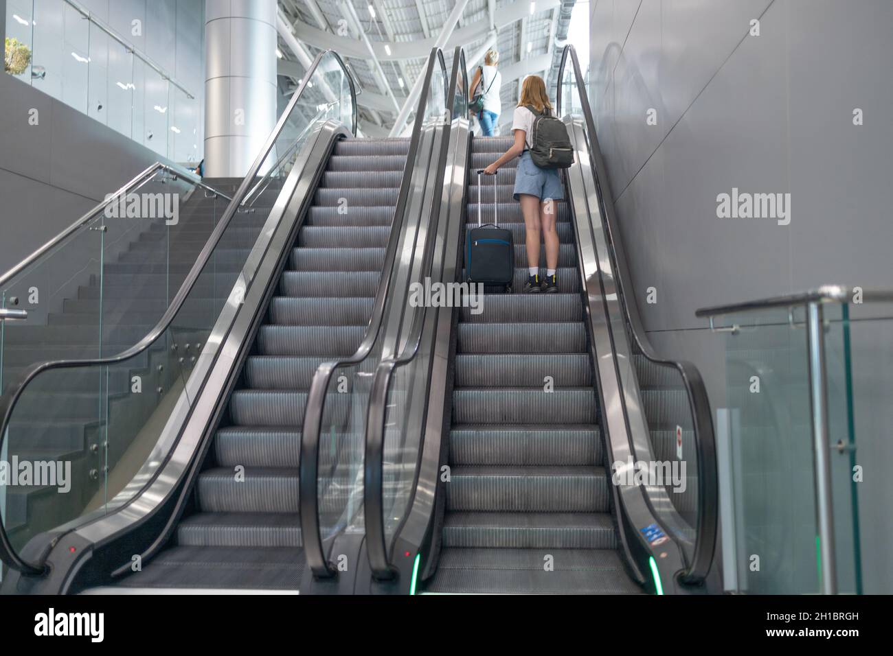 Tourist im Flughafenterminal, der an der Rolltreppe steht. Passagierin, die während einer Covid19-Virus-Pandemie mit dem Flugzeug unterwegs ist Stockfoto