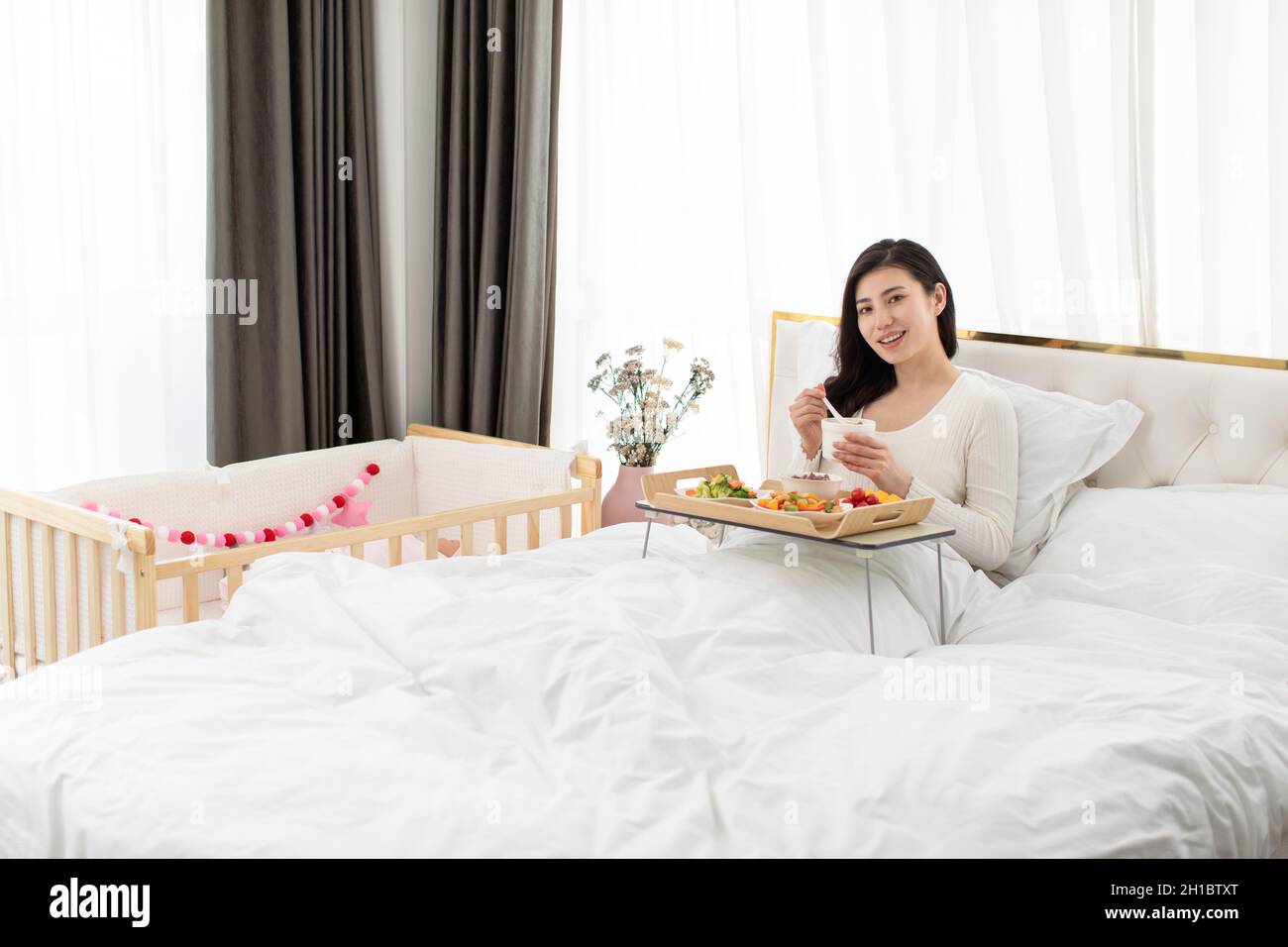 Glückliche junge Mutter beim Essen im Bett Stockfoto