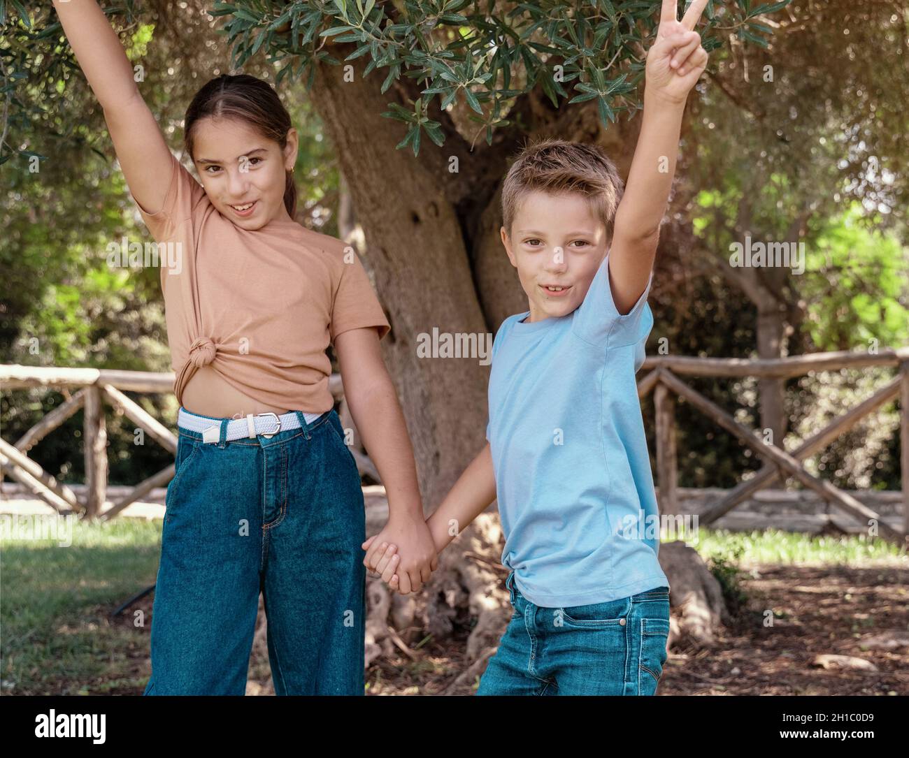 Glücklicher Bruder und Schwester halten sich die Hände und zeigen V gest im Freien. Nettes Kind Mädchen und Junge Spaß in einem Park im Sommer. T-Shirt-Modell Stockfoto