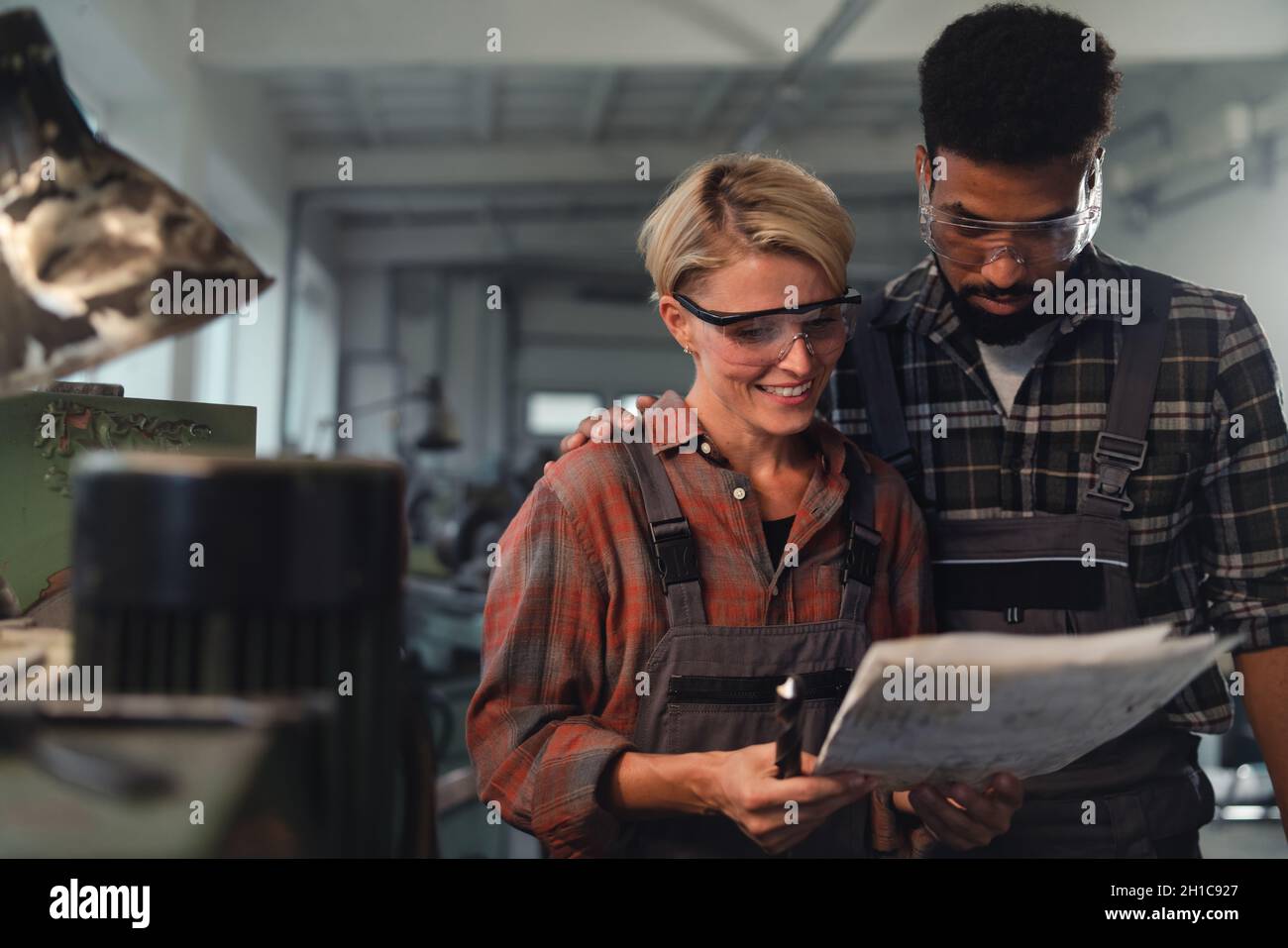 Porträt junger birazialer Industriekollegen, die in Innenräumen in einer Metallwerkstatt arbeiten, lächelnd. Stockfoto