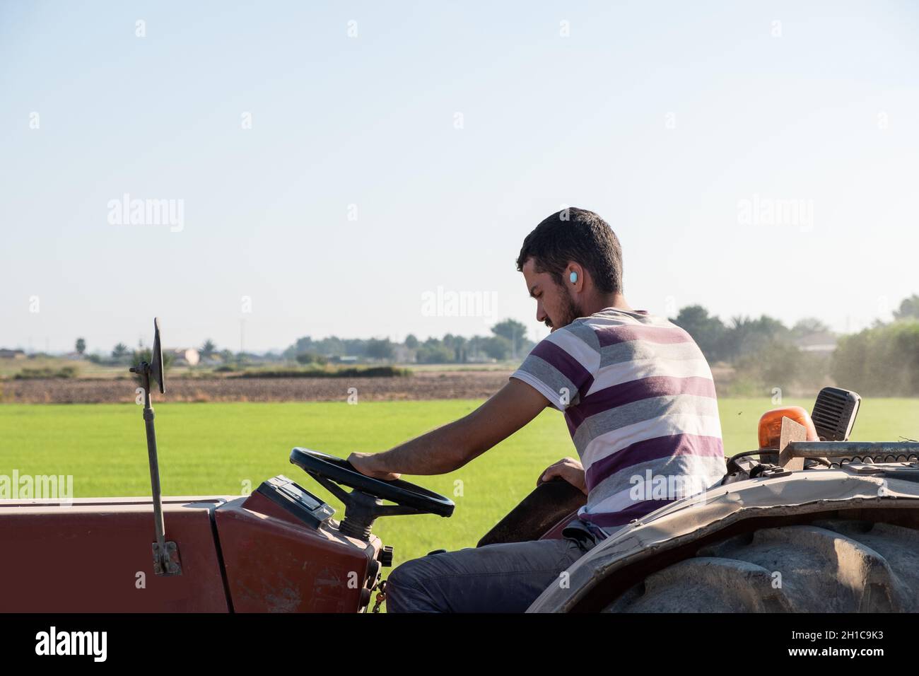 Junger Bauer pflügt mit einem Traktor, während er Musik hört. Stockfoto