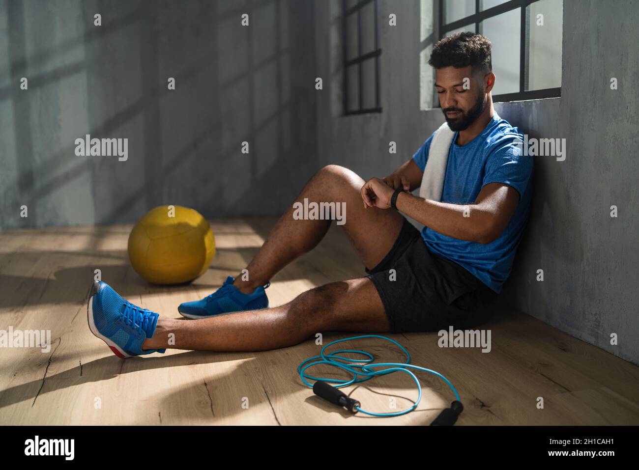 Der junge afroamerikanische Sportler sitzt und nutzt die Smartwatch im Fitnessstudio, beim Workout Stockfoto