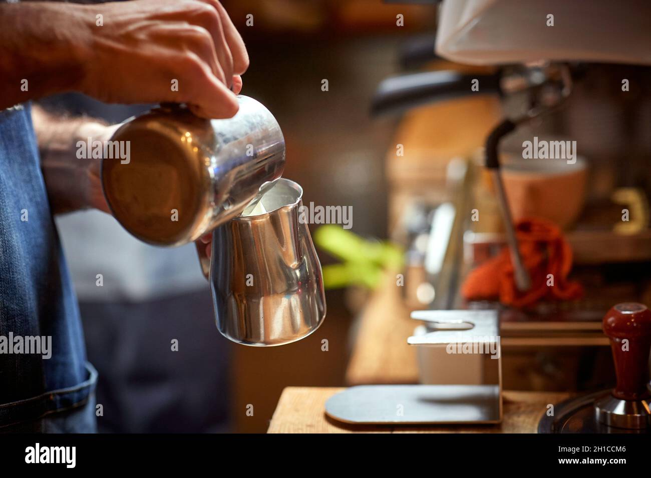 Ein Barkeeper bereitet eine Milch zu, um im Gerät einen aromatischen und duftenden Espresso zuzubereiten. Kaffee, Getränke, Bar Stockfoto