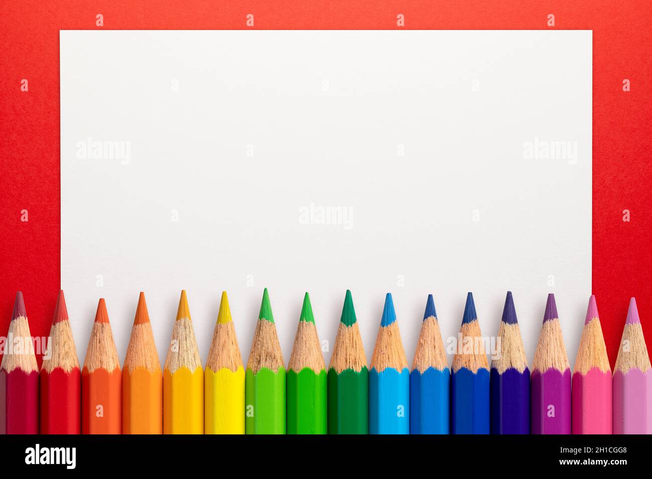 Rahmen aus Farbstiften und weißem Papier auf rotem Hintergrund. Stockfoto