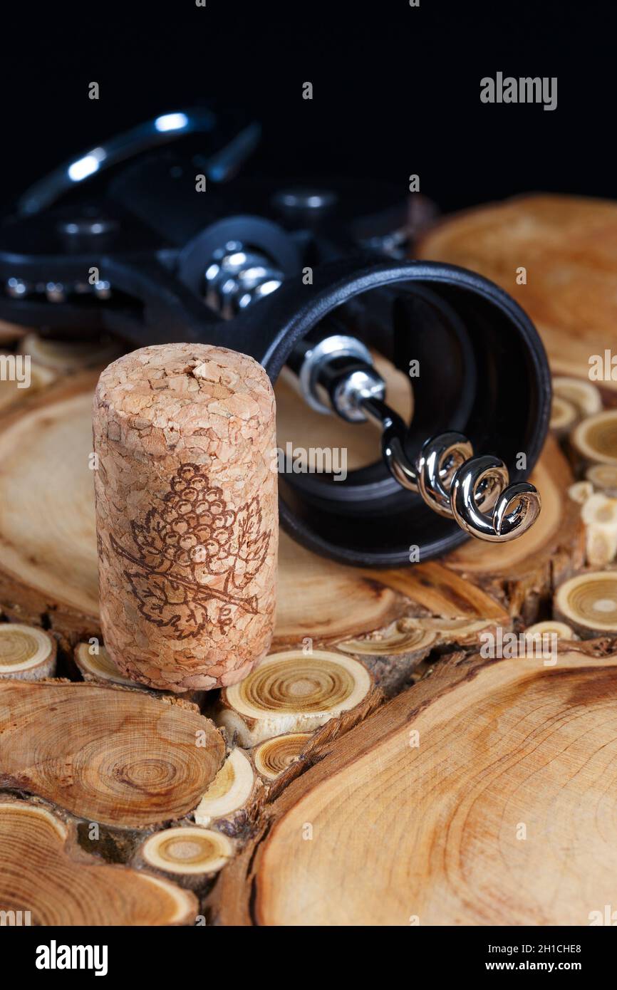 Kork und Korkenzieher auf einem Brett aus Holzschnitten, auf schwarzem Hintergrund, mit geringer Schärfentiefe Stockfoto