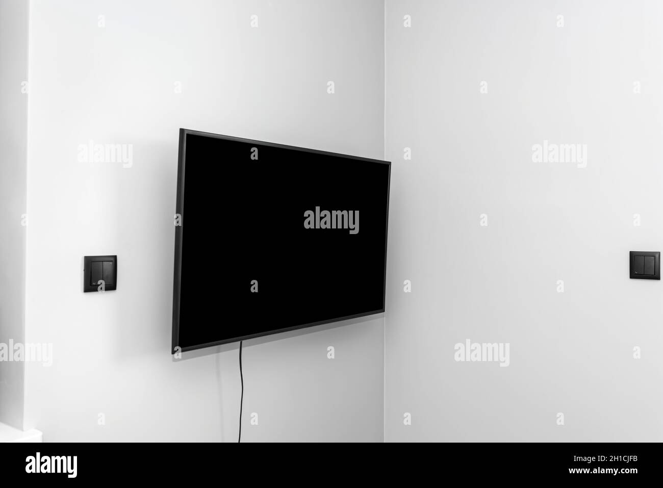 Der Fernseher ist an der grauen Wand im Schlafzimmer aufgehängt, die Knöpfe für die Jalousien sind sichtbar. Stockfoto