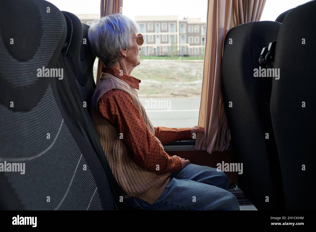 Ältere Frau in legerer Kleidung, die durch das Fenster schaut, während sie mit dem Intercity-Bus unterwegs ist Stockfoto