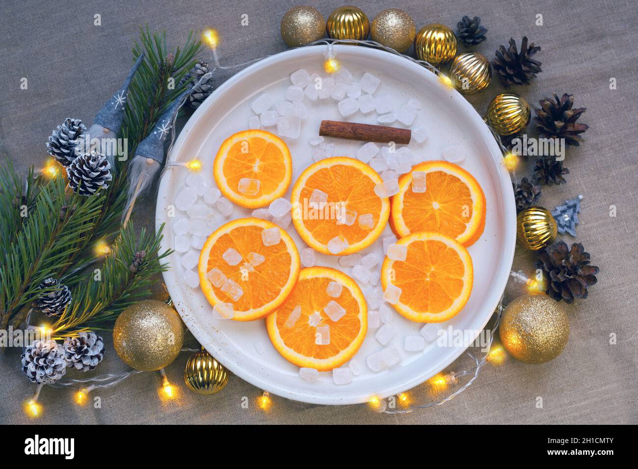 Orangen am Teller in der Nähe von christbaumzweig, goldene Kugeln und Pinienzapfen. Mandarinen-Verzierungen Stockfoto