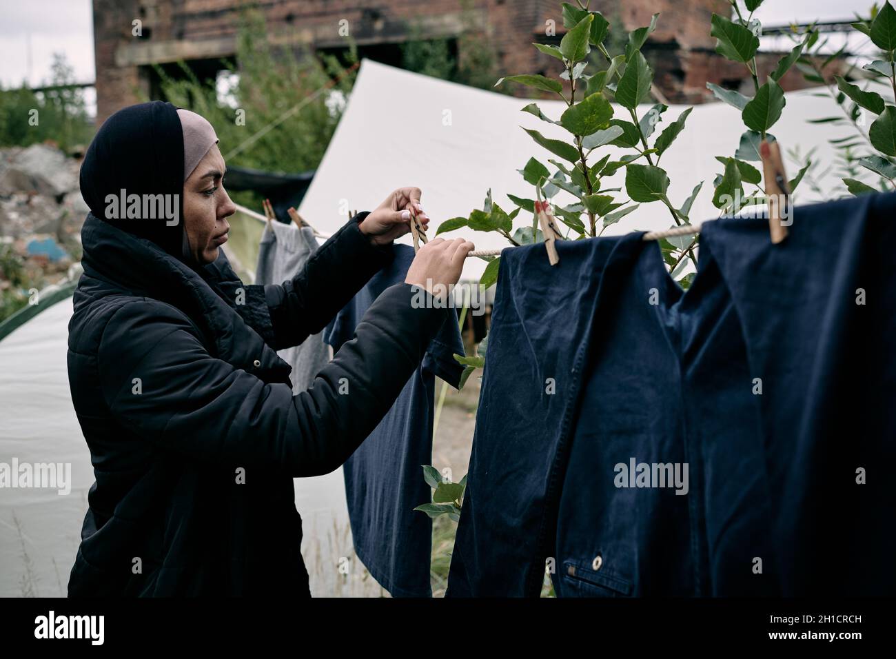 Junge Migrantinnen hängen saubere Kleidung an einem Seil gegen die Besiedlung im Lager Stockfoto