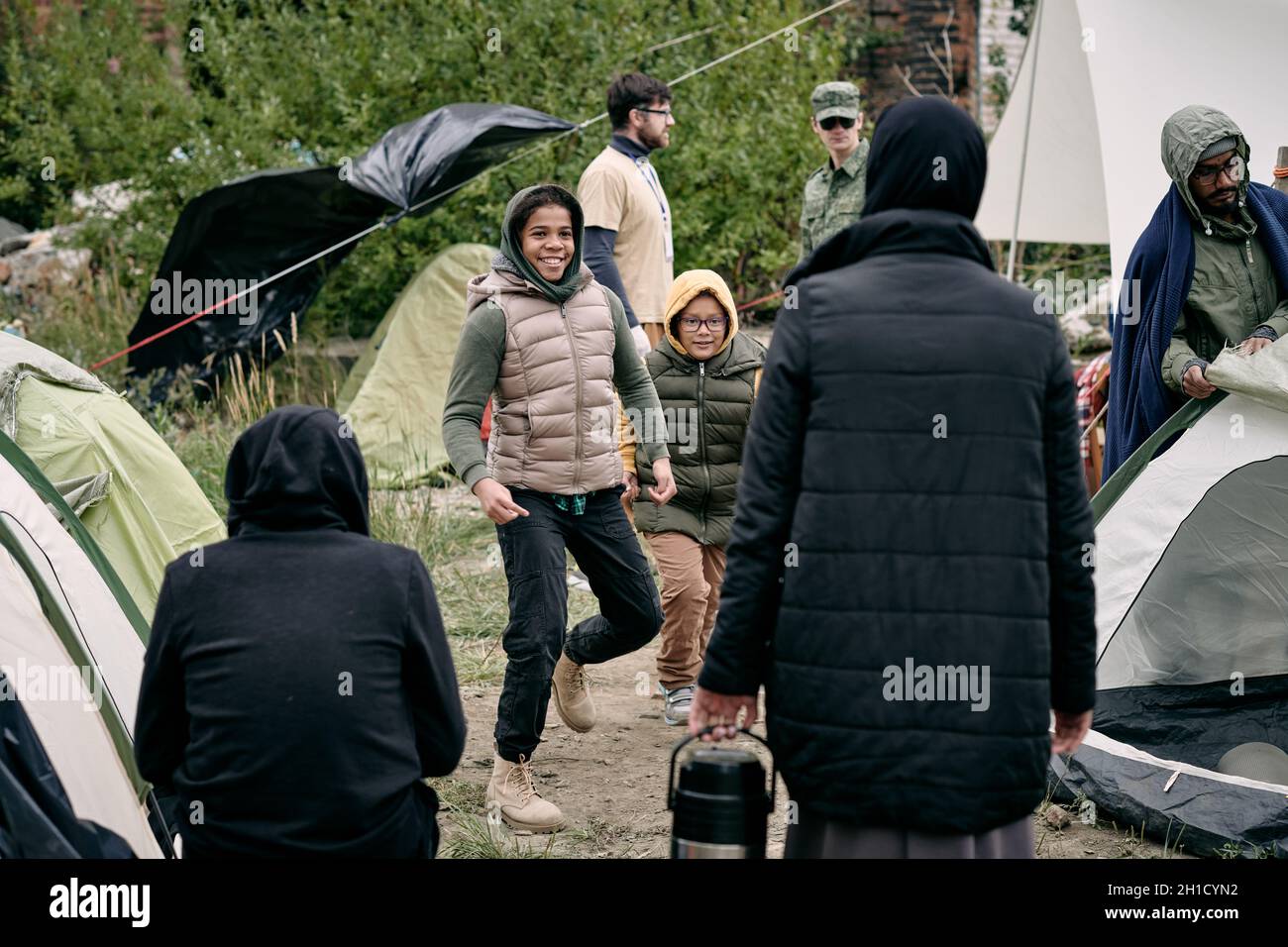 Glückliches entzückendes Mädchen, das vor ihrer Familie zwischen Zelten des Flüchtlingslagers tanzt Stockfoto