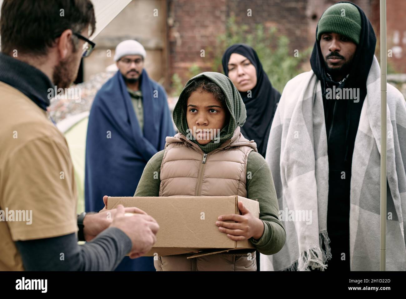 Ernsthaftes afroamerikanisches Mädchen mit verpackter Schachtel, das vor ihr einen männlichen Freiwilligen ansieht Stockfoto