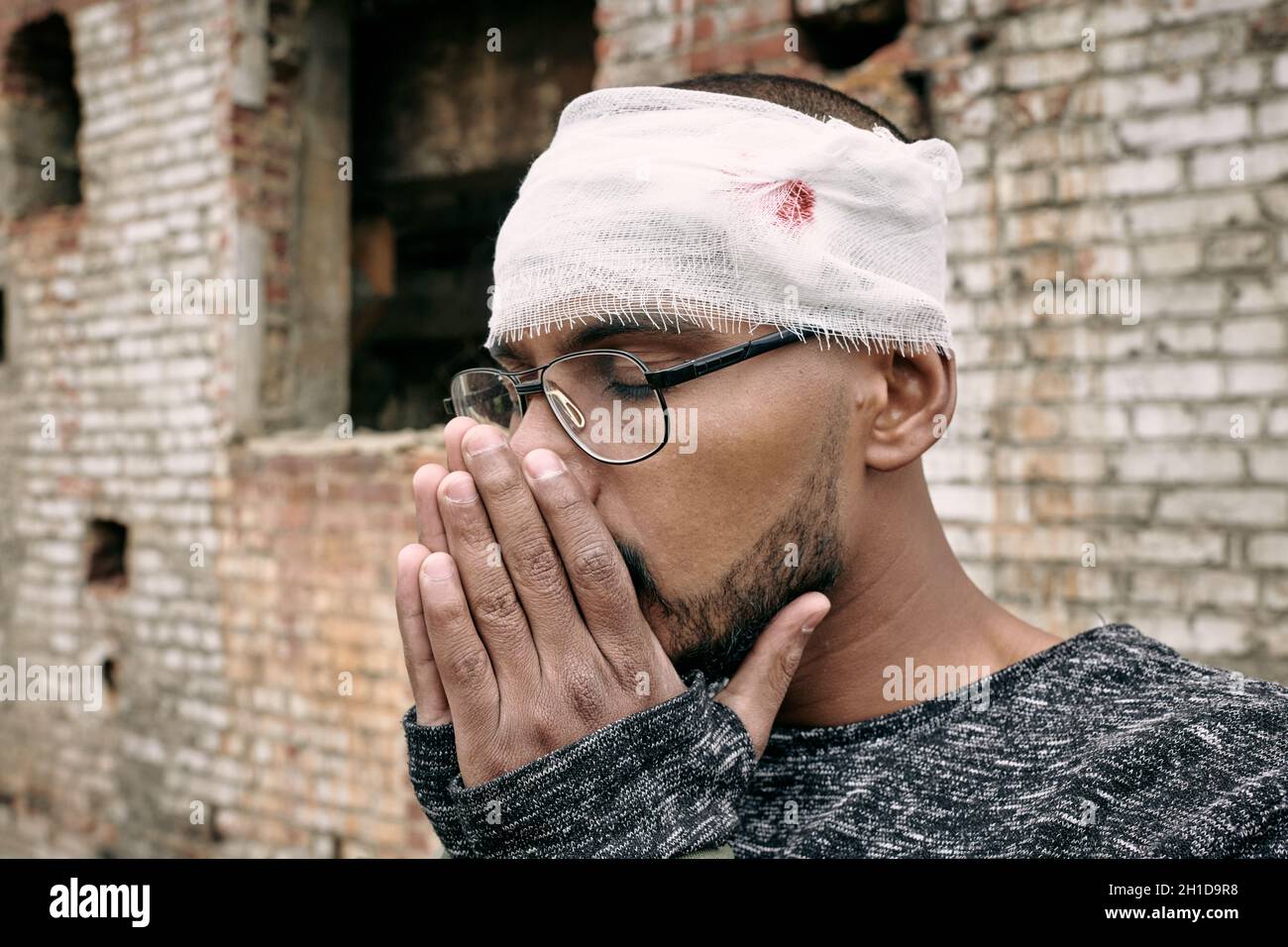 Junger verwundete männliche Flüchtling mit Verband um den Kopf herum, wobei die Hände dicht an sein Gesicht gelegt wurden Stockfoto