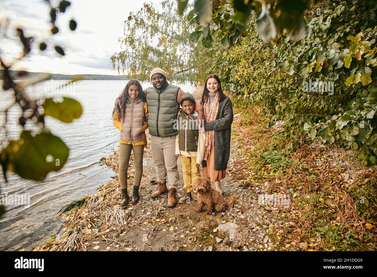 Porträt einer glücklichen vierköpfigen Familie, die die Kamera umarmt und lächelt, während sie gemeinsam im Herbstwald spazieren geht Stockfoto