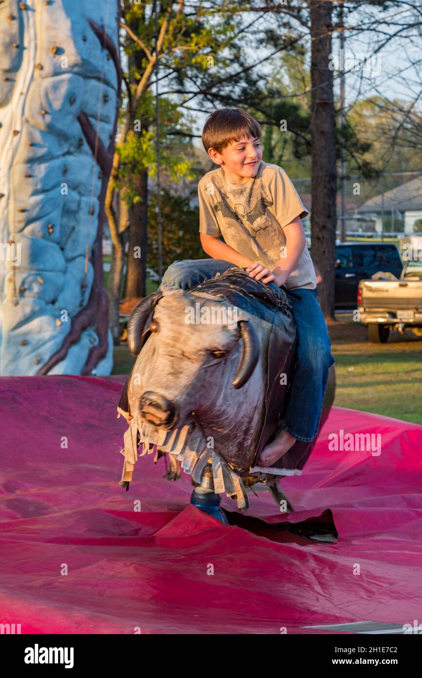 Kleiner Junge, der auf der Pine Hills Festival Street Fair in Stone County, Mississippi, einen mechanischen Bullen reitet Stockfoto