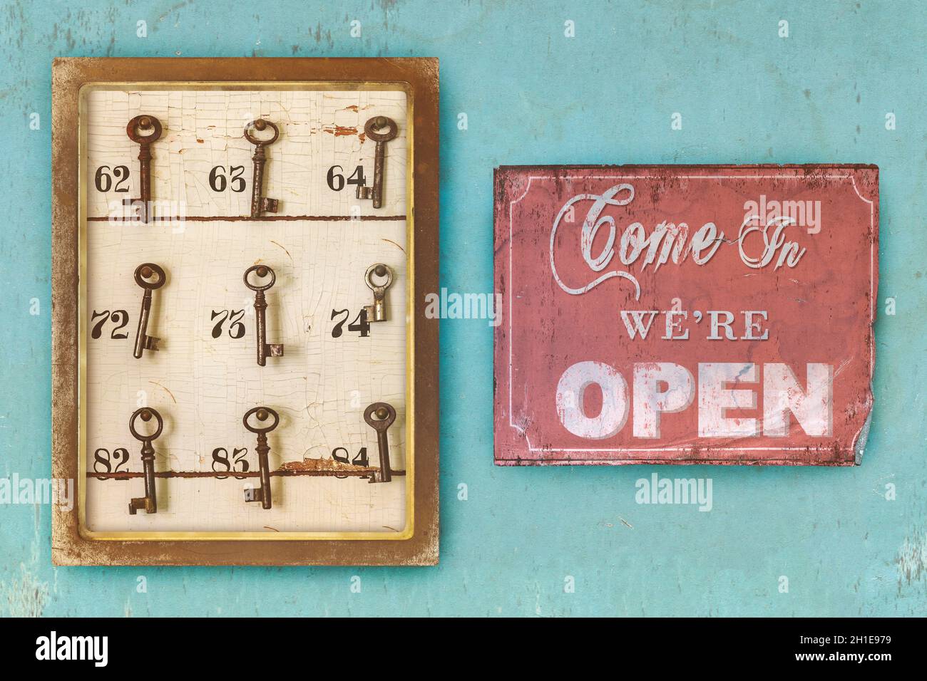 Kleines Vintage-Kabinett mit verrosteten Hotelschlüsseln und Zimmernummern und kommen herein wir sind offenes Schild auf einem blau erodierten Hintergrund Stockfoto