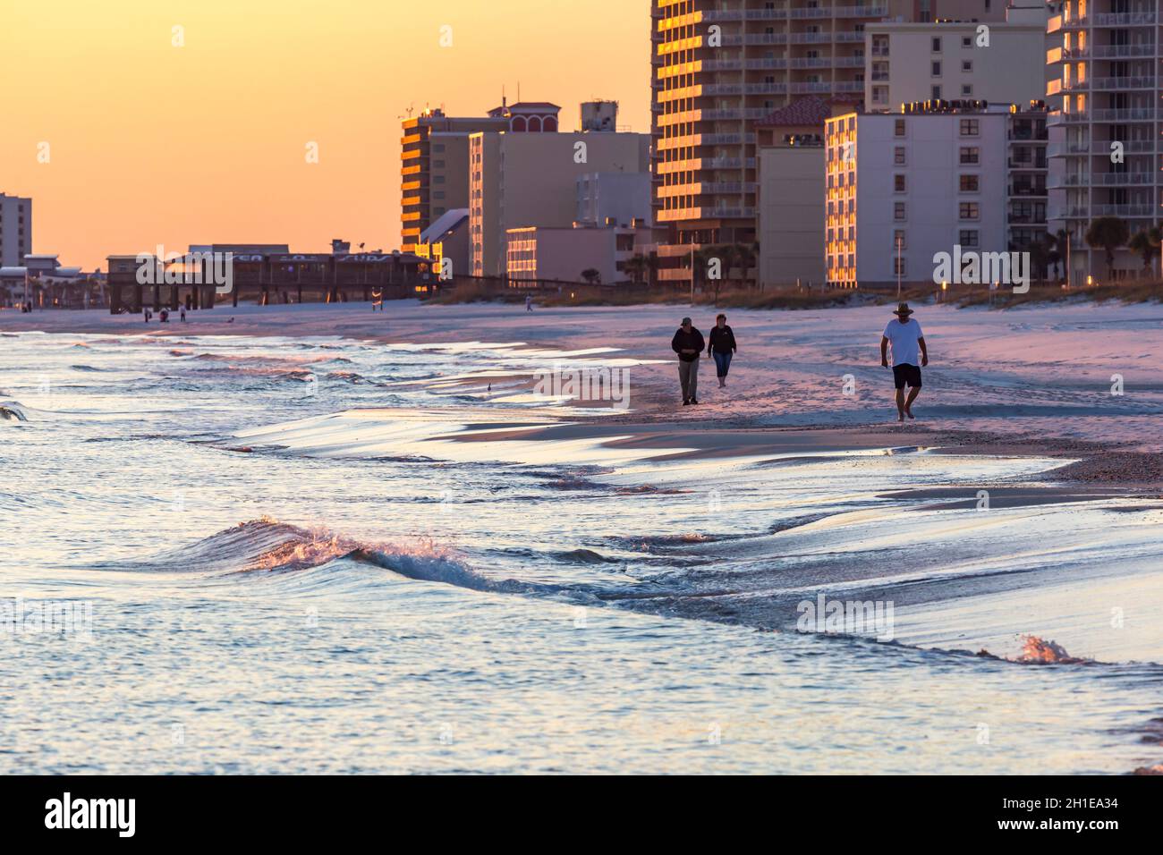 Leute, die abends am Strand spazieren gehen, vor Hotels und Wohnanlagen in der Nähe des Sonnenuntergangs in Gulf Shores, Alabama Stockfoto