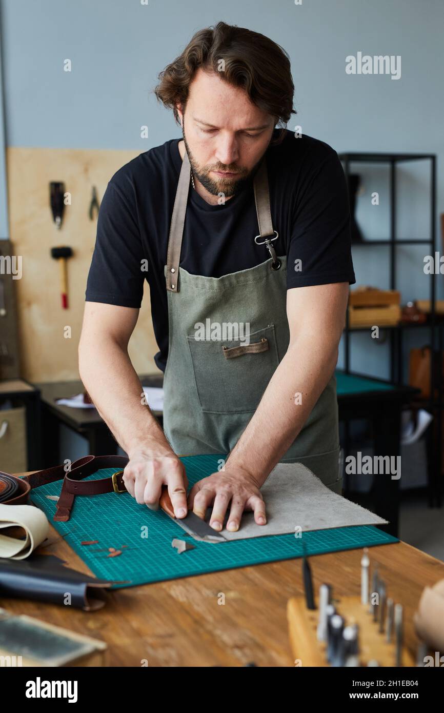 Vertikales Porträt eines bärtigen männlichen Kunsthandwerkers, der im Werkstattstudio mit Leder arbeitet, Konzept für kleine Unternehmen Stockfoto
