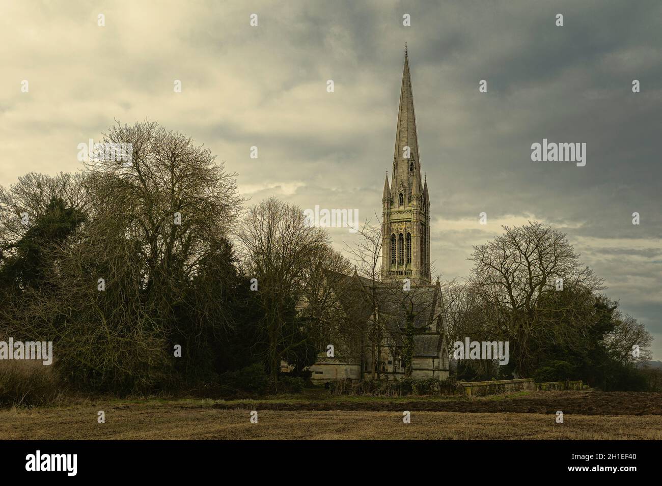 Ländliche englische Szene mit einer alten Kirche mit einem wunderschönen Kirchturm, der im Winter von Bäumen und Ackerland flankiert wird, und einem hellen Himmel in South Dalton, Yorkshire, Großbritannien. Stockfoto