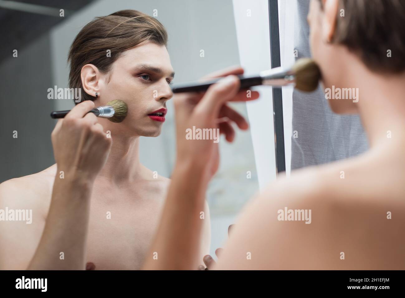 Junger Transgender-Mann, der Gesichtspuder in der Nähe des Spiegels anwendet Stockfoto