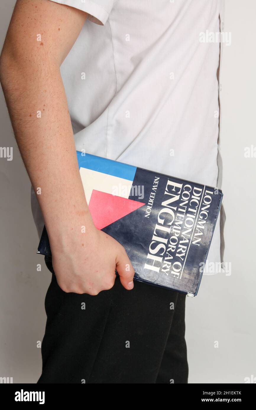 Schuljunge trägt Longmans Wörterbuch des Zeitgenössischen Englischen unter Arm Stockfoto