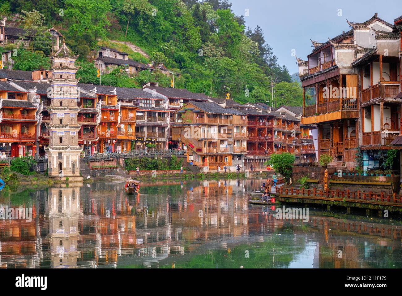 FENGHUANG, CHINA - 22. APRIL 2018: Feng Huang Ancient Town (Phoenix Ancient Town) am Tuo Jiang Fluss mit dem Wanming Pagodenturm und Touristenboot in der Sonne Stockfoto