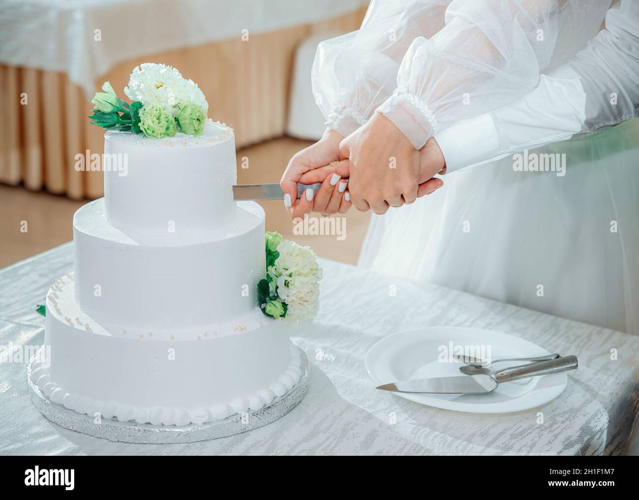 Frisch verheiratetes Paar schneidet den Hochzeitstorte. Eine Braut und ein Bräutigam Hände halten ein Messer, Nahaufnahme. Wunderschöne weiße dreistufige Torte mit Blumen verziert Stockfoto