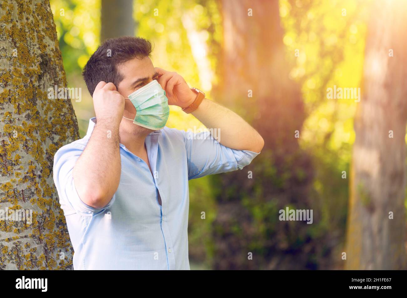 Junger Mann, der im Park steht, entfernt eine schützende Gesichtsmaske und feiert den Sieg über das Coronavirus draußen unter freiem Himmel. Ende der Quarantäne. Maske entfernen. Stockfoto