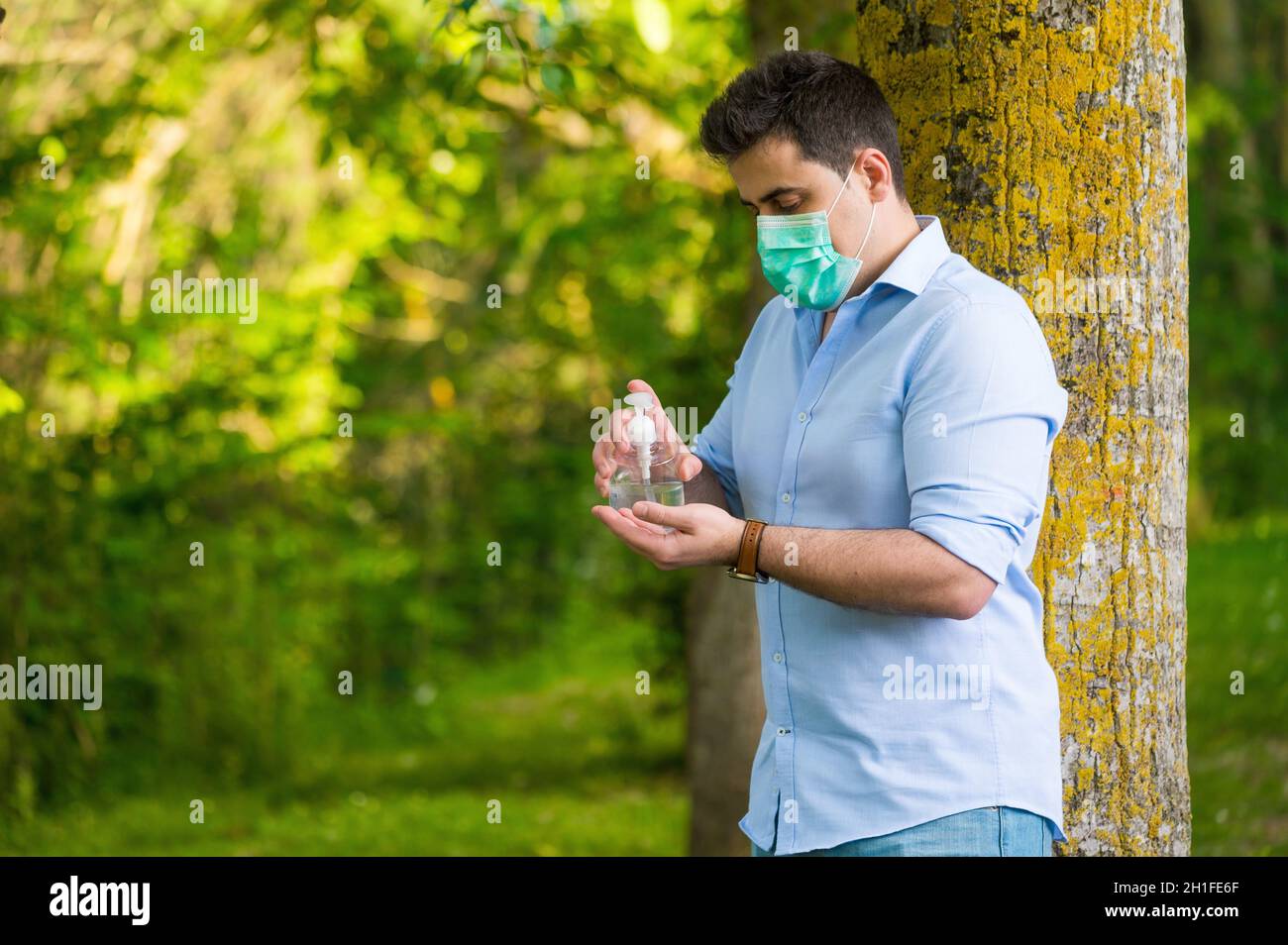 Mann mit Schutzmaske im Park stehend, mit Waschhandalkohol-Gel, gegen Coronavirus-Krankheit Covid-19 . Antiseptikum, Hygiene und Gesundheit Stockfoto