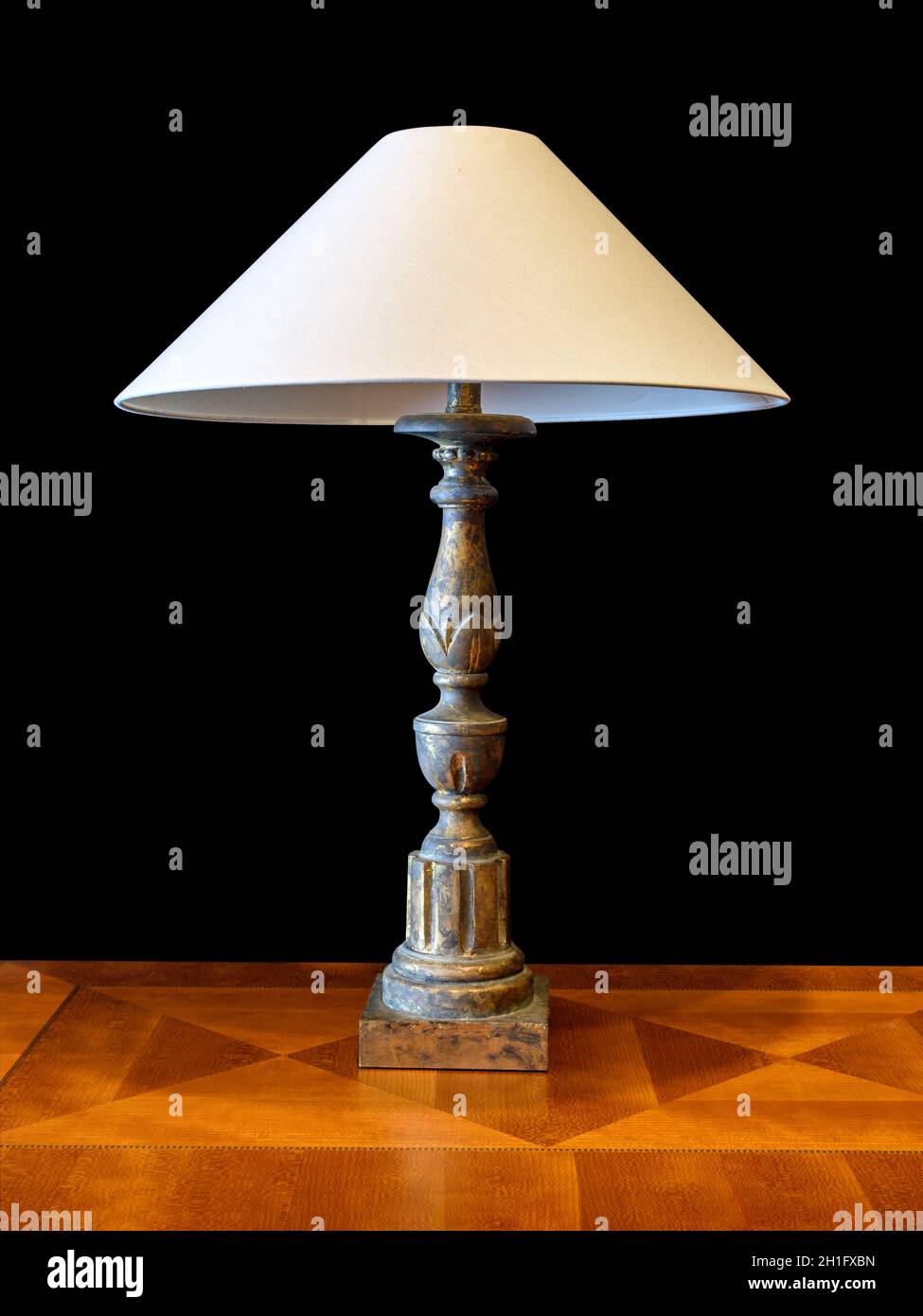 Alte Patina-Lampe aus Messing mit Lampenschirm aus Stoff, auf braunem Holz mit geometrischem Furnier. Isoliert auf schwarzem Hintergrund, Beschneidungspfad angeschlossen Stockfotografie