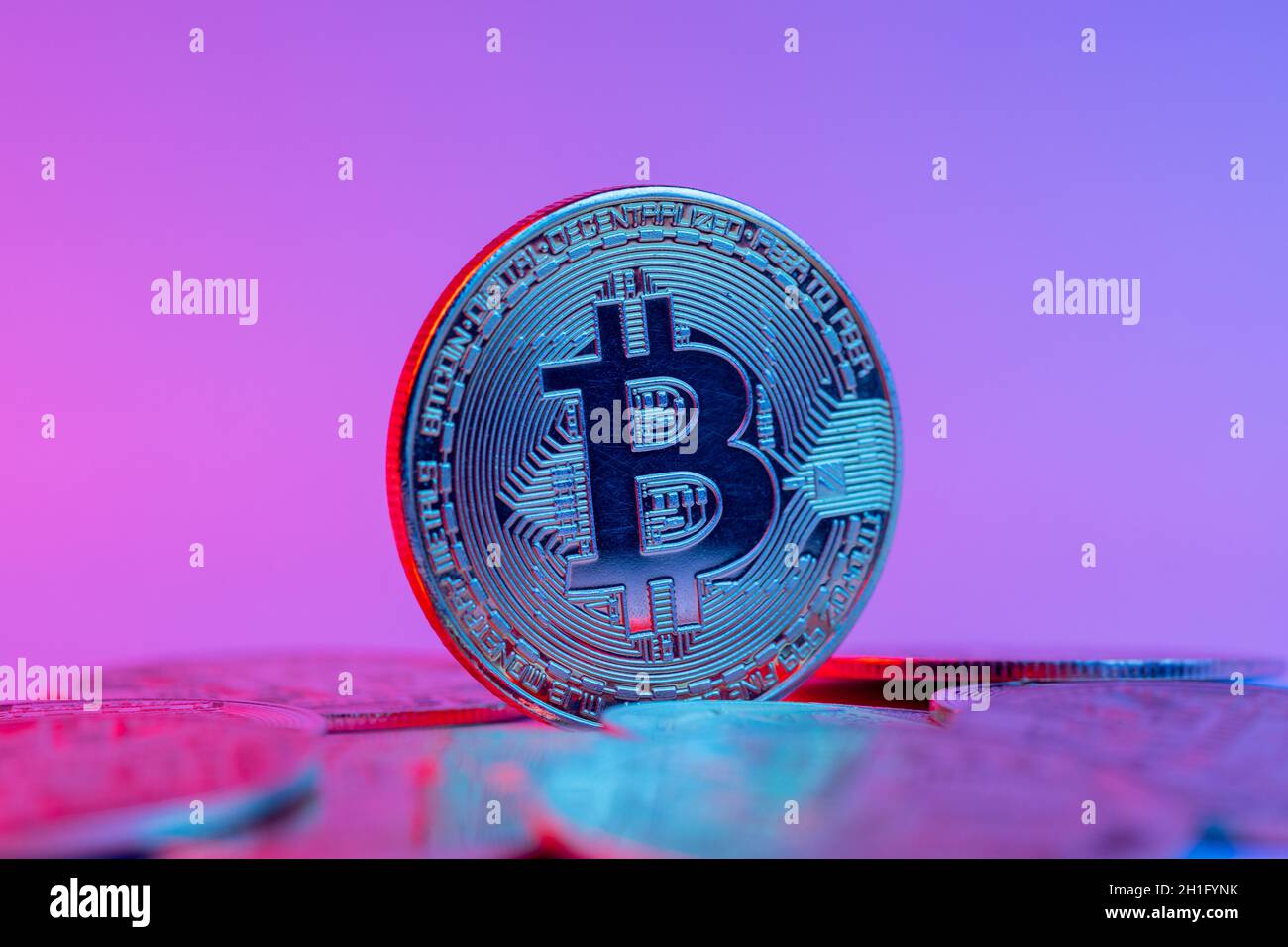Bitcoin auf einem Haufen Kryptowährungs-Goldmünzen. Das Neonlicht der Zukunft ist rot und blau. Stockfoto