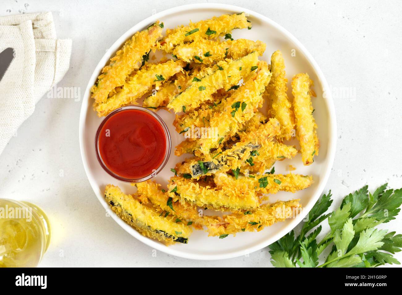 Knusprig gebratene Zucchini-Sticks mit Paniermehl und Tomatensoße auf dem Teller auf hellem Steingrund. Draufsicht, flach liegend Stockfoto