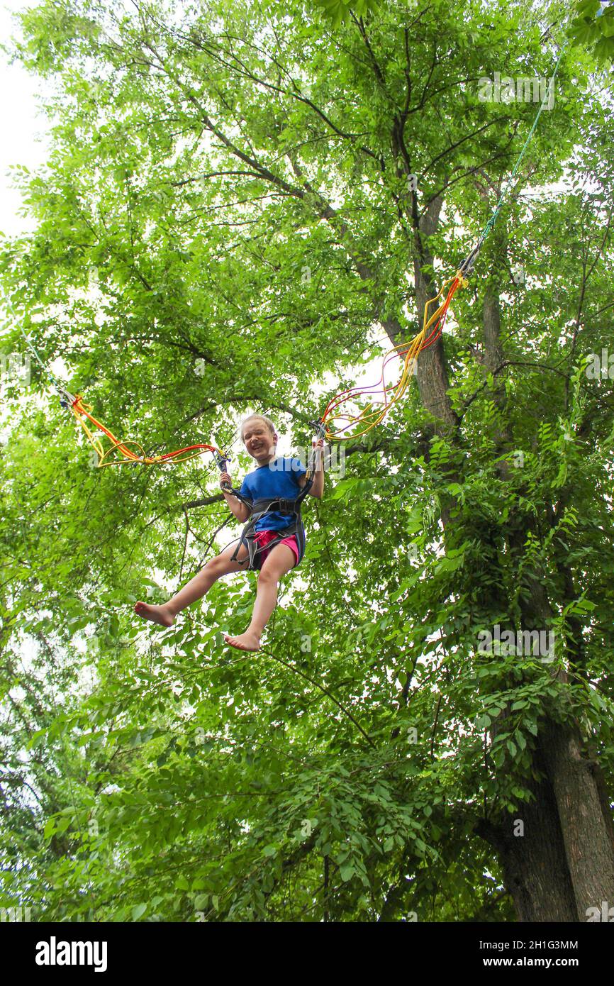 Das lächelnde Mädchen springt mit Bungee im Trampolin im Park gegen grüne Bäume Stockfoto