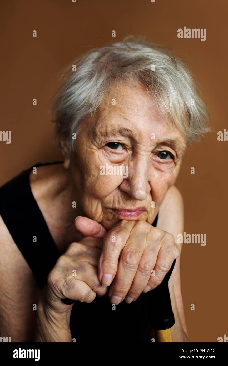 Das Gesicht und die Augen einer alten traurigen Frau. Sie sitzt zu Hause und schaut zur Kamera. Konzept der menschlichen Probleme und Emotionen. Selektiver Fokus auf die Hände Stockfoto