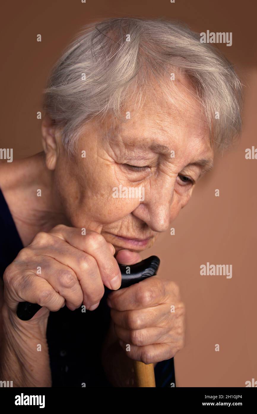 Das Gesicht und die Augen einer alten traurigen Frau. Sie saß zu Hause und schaute nach unten. Konzept der menschlichen Probleme und Emotionen. Selektiver Fokus auf die Hände Stockfoto
