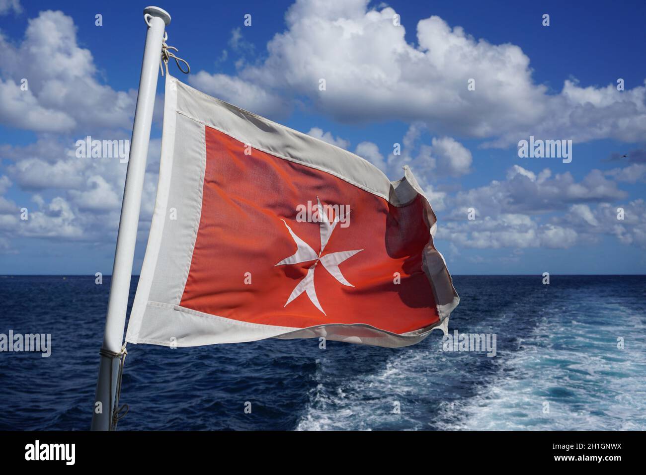 Alte maltesische Flagge. Weißes Kreuz auf rotem Hintergrund, das am Heck des im Mittelmeer fahrenden Schiffes fliegt.Foto: Willy Matheisl Stockfoto