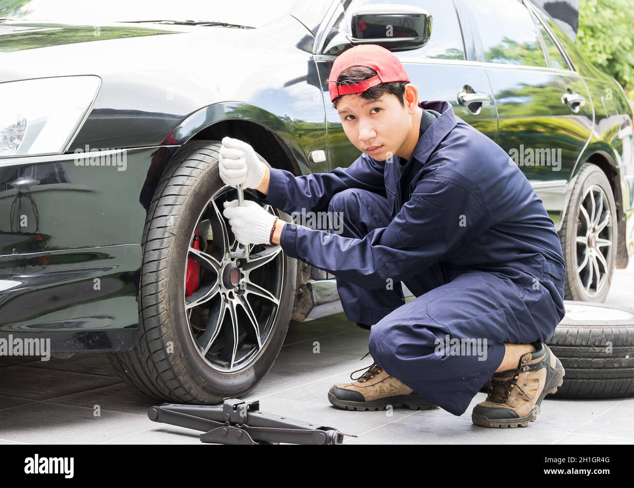 Junge Mechaniker in Uniform ersetzen die Radmuttern mit der Hand beim Wechseln der Reifen am Fahrzeug Stockfoto