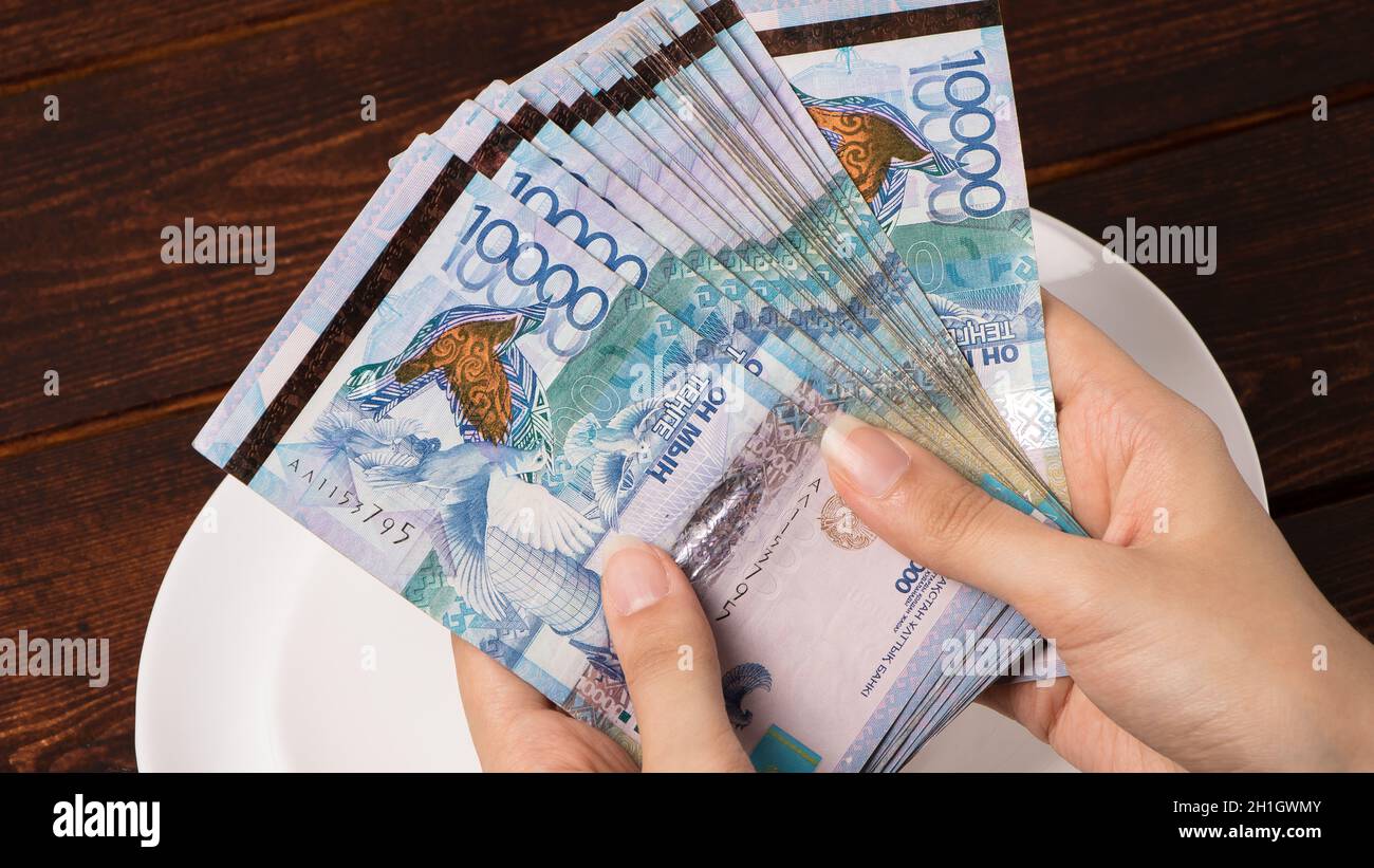 Zählen Sie Geld in Tenge. Viele kasachische Tenge auf einem weißen Teller. Die nationale Währung von Kasachstan. Gehalt in Tenge. Um das Budget zu kürzen. Stockfoto