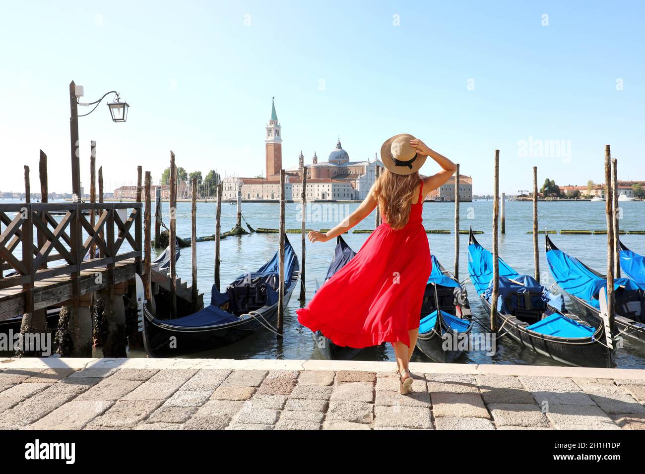 Urlaub in Venedig. Rückansicht von schönen Mädchen in roten Kleid genießen Blick auf die Lagune von Venedig mit der Insel San Giorgio Maggiore und Gondeln moore Stockfoto