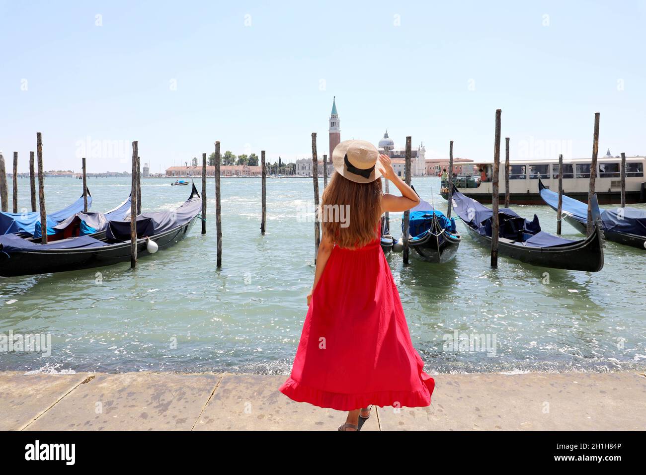 Urlaub in Venedig. Rückansicht von schönen Mädchen in langen roten Kleid genießen Blick auf die Lagune von Venedig mit der Insel San Giorgio Maggiore und Gondeln Stockfoto