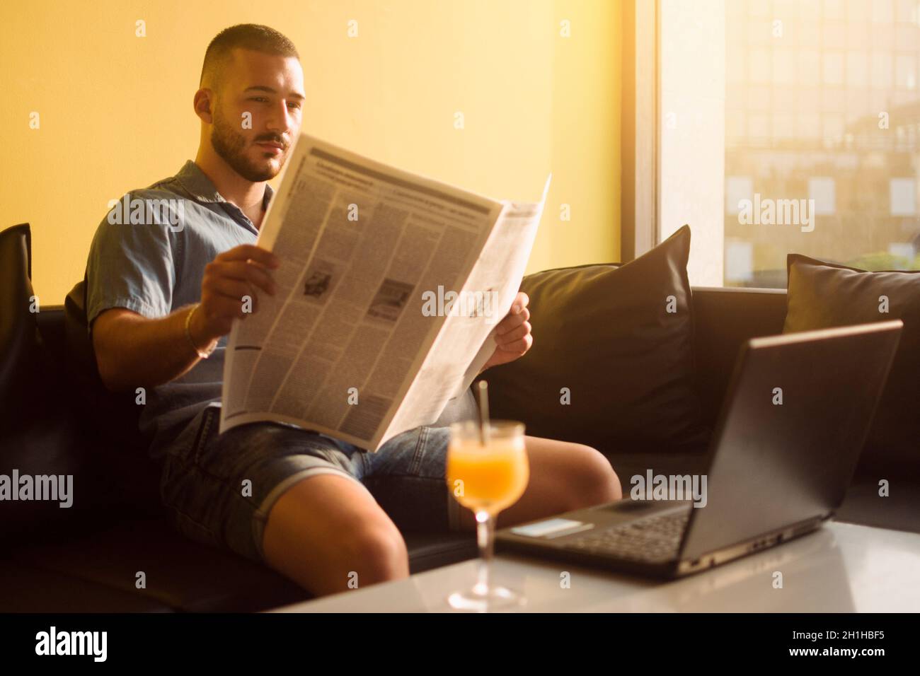 Der junge Mann liest Zeitung im Café auf gelbem Hintergrund. Stockfoto
