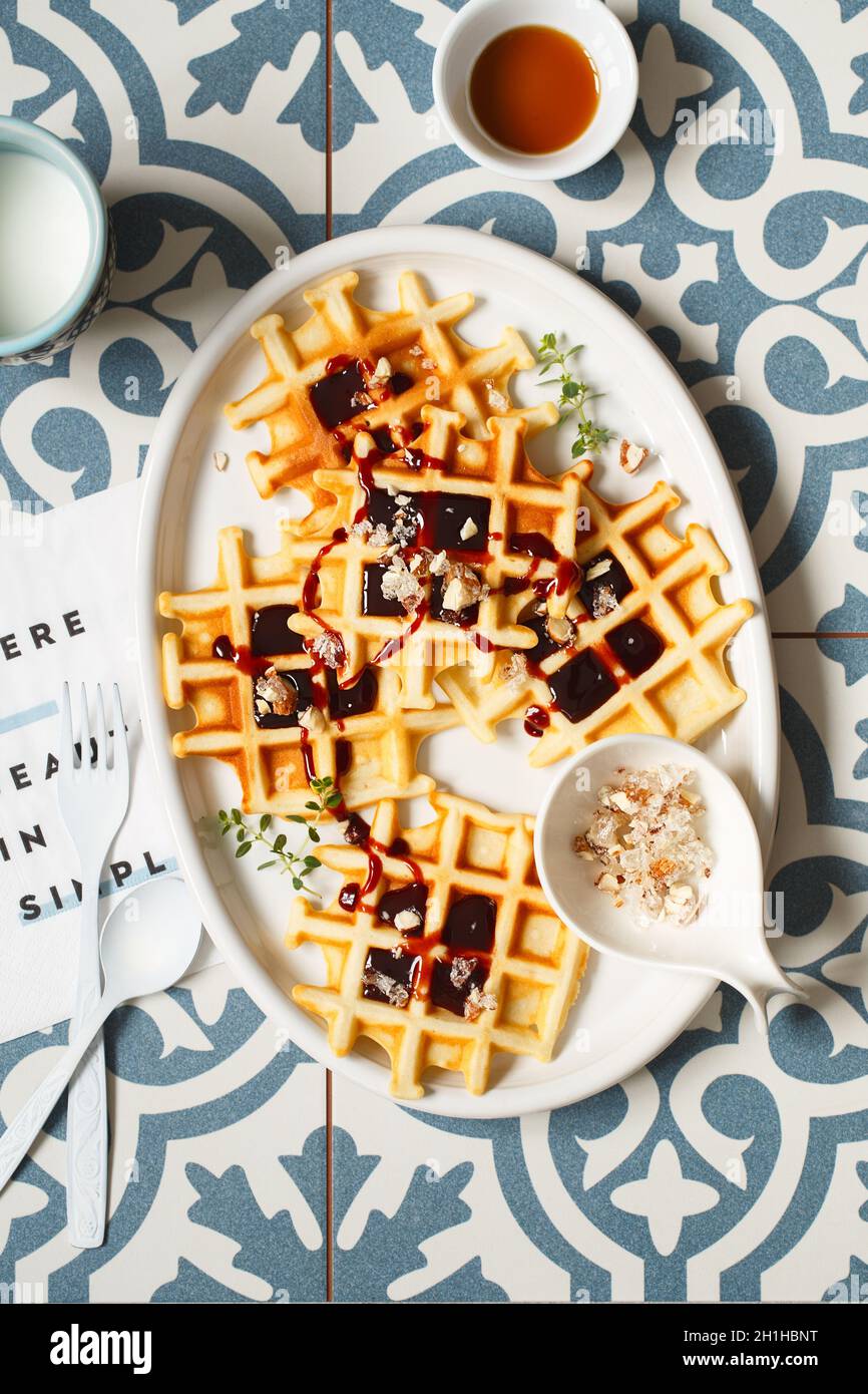 Belgische oder Brüsseler Waffeln mit Dattelsirup oder Marmelade und kandierten gerösteten Nüssen. Hausgemachte Waffeln in einem weißen ovalen Teller auf dem Küchentisch. Traditionell Stockfoto