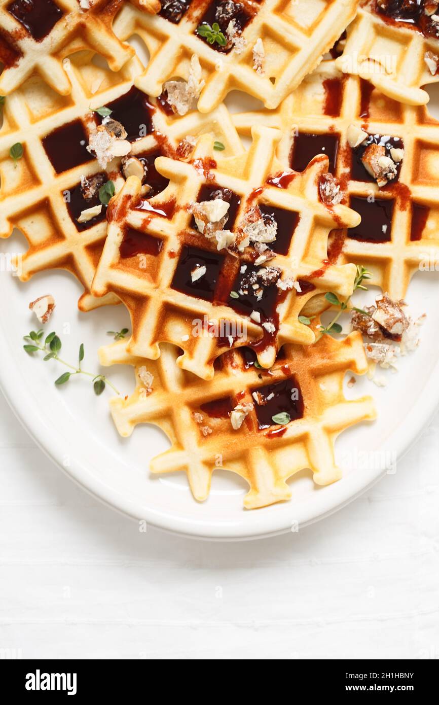 Belgische oder Brüsseler Waffeln mit Dattelsirup oder Marmelade und kandierten gerösteten Nüssen. Hausgemachte Waffeln in einem weißen ovalen Teller auf dem Küchentisch. Traditionell Stockfoto