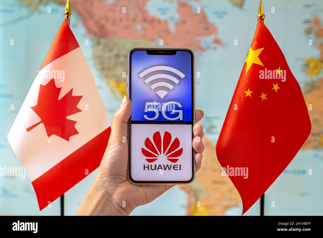 Calgary, Alberta, Kanada. September 2020. Eine Person, die ein iPhone mit einem 5G- und Huawei-Logo auf dem Bildschirm neben einer Kanada- und China-Flagge auf einer Welt hält Stockfoto