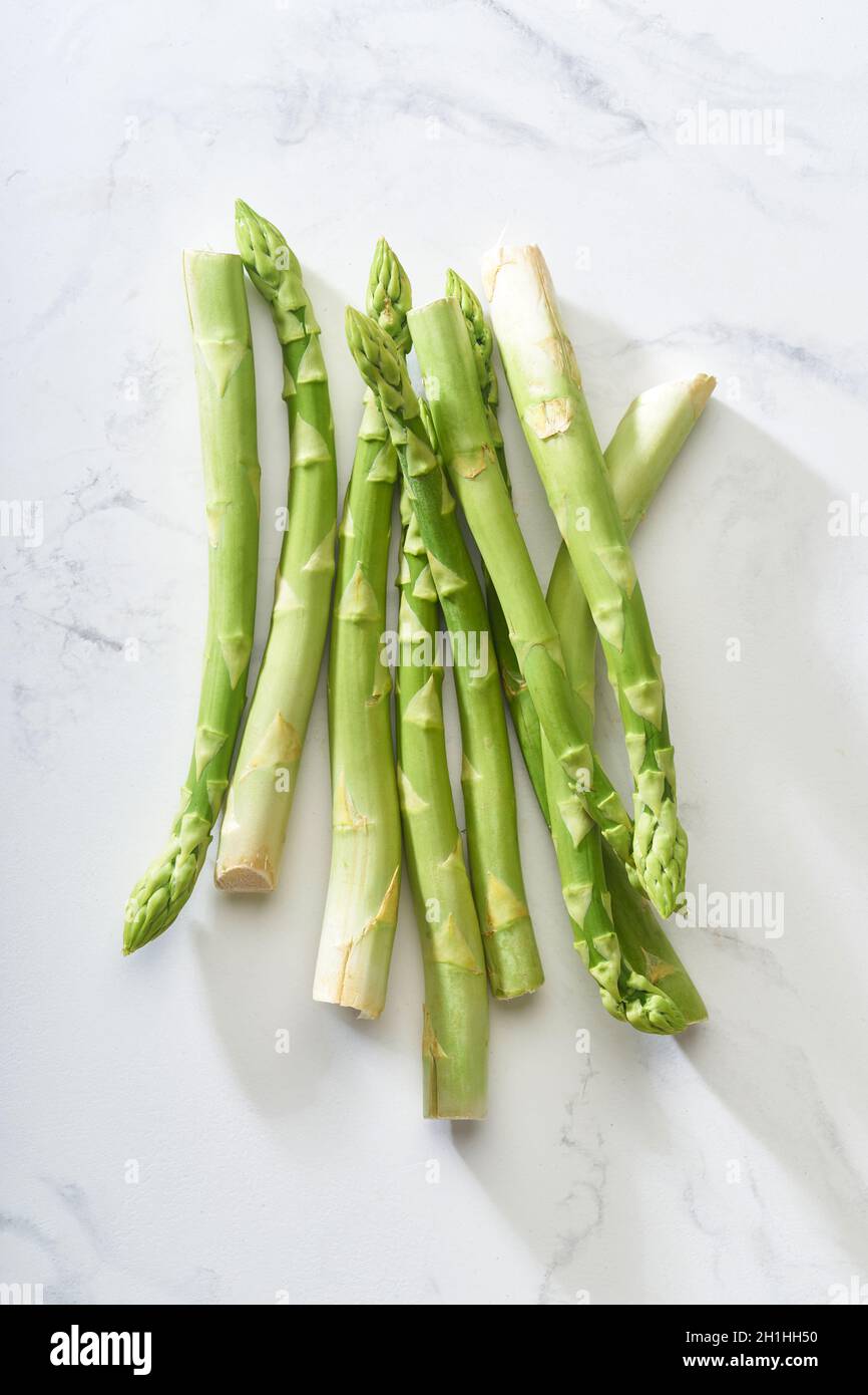 Frischer grüner Spargel auf weißem Marmortisch. Flat Lay mit veganer Lebensmittelzutat gesundes Essen von oben Stockfoto