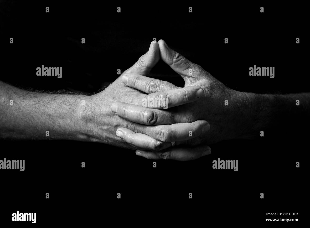 Schwarz-weißes Bild von männlichen Händen, die ausgehalten wurden, mit Daumen zusammengehalten, in Gedanken oder im Gebet, isoliert vor einem schwarzen Hintergrund mit dramatischem Seufzen Stockfoto