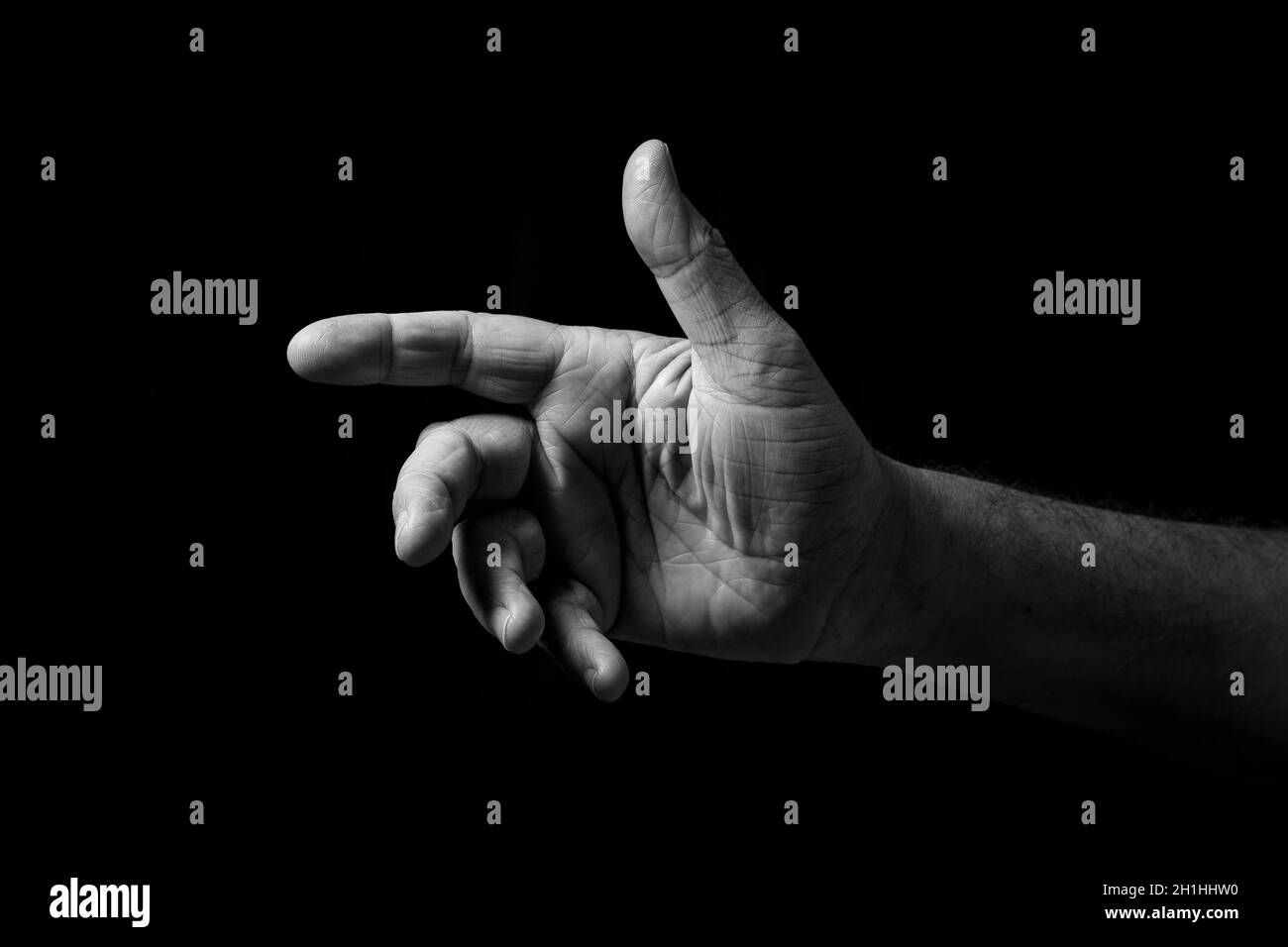 Schwarz-Weiß-Bild mit faltiger männlicher Hand, die mit offener Handfläche nach außen zeigt, isoliert vor einem schwarzen Hintergrund mit dramatischer Beleuchtung. Stockfoto