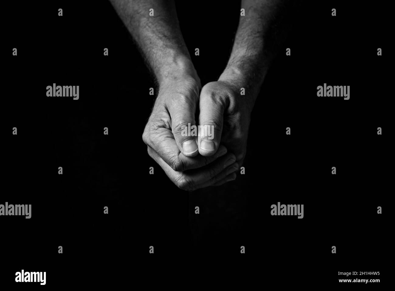 Schwarz-weißes Bild von zerknitterten männlichen Händen, die in Gedanken oder im Gebet zusammengehalten und vor einem schwarzen Hintergrund mit dramatischem Licht isoliert wurden Stockfoto