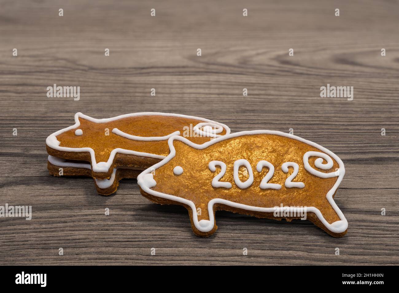Niedliche Lebkuchenferkel für glückliches Neujahr 2022 auf einem braunen Holzhintergrund gestapelt. Nahaufnahme von goldgebackenen verzierten Plätzchen - Schweinchen für Viel Glück. Stockfoto
