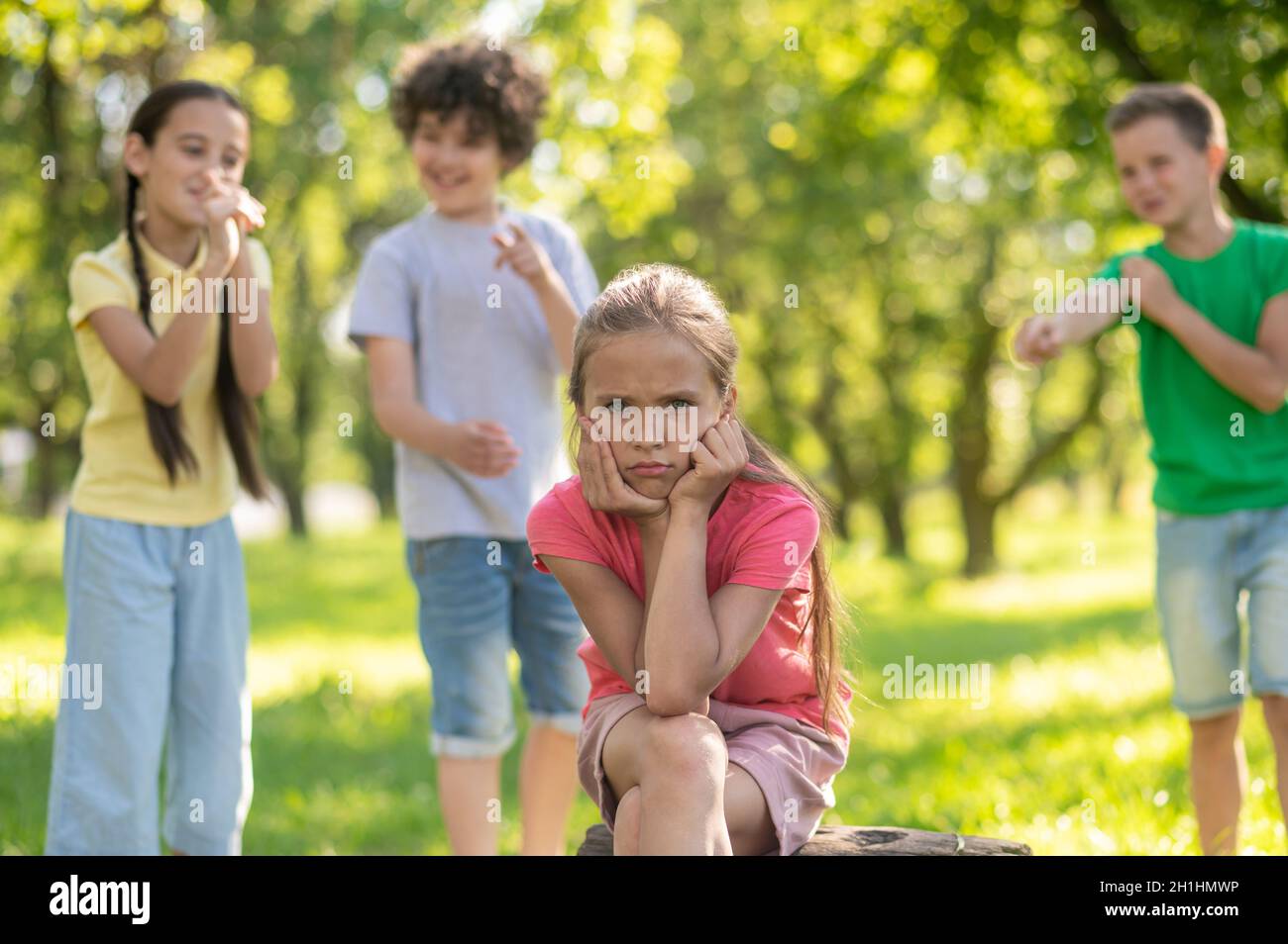 Trauriges Mädchen und Kinder, die sich im Freien verspotten Stockfoto