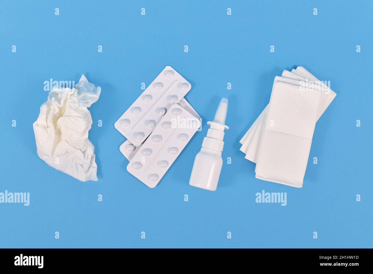 Draufsicht auf Nasensprayflasche, Medikamentententabletten und verwendetes Gewebe, das während der Erkältung auf blauem Hintergrund verwendet wird Stockfoto